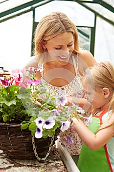 Mother And Daughter Growing Plants In Greenhouse