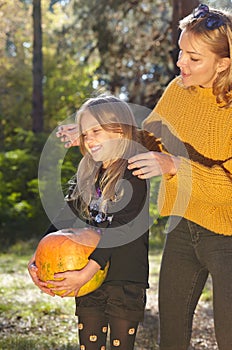 Mother and daughter at Halloween forest. Cute little child with a pumpkin posing in autumn park
