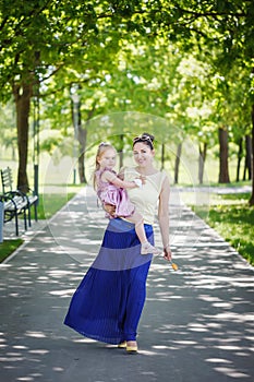 Mother with the daughter on hands walk in summer park in sunny