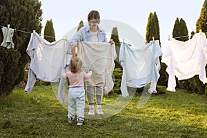 Mother and daughter hanging clothes with clothespins on washing line for drying in backyard, back view