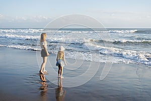 Mother with daughter have fun at beach with black sand in Bali, running at waves, enjoy life and traveling.