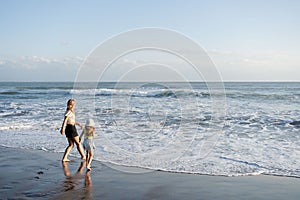 Mother with daughter have fun at beach with black sand in Bali, running at waves, enjoy life and traveling.