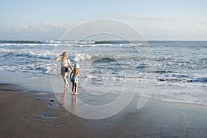 Mother with daughter have fun at beach with black sand in Bali, running at waves, enjoy life and traveling.