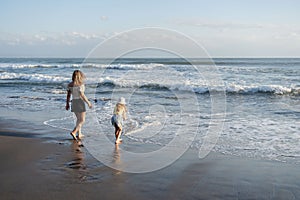 Mother with daughter have fun at beach with black sand in Bali, running at waves, enjoy life and traveling.