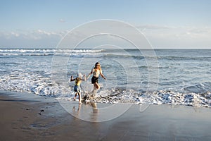 Mother with daughter have fun at beach with black sand in Bali, running at waves, enjoy life and traveling.