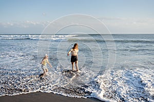 Mother with daughter have fun at beach with black sand in Bali, running at waves, enjoy life and traveling.