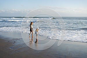 Mother with daughter have fun at beach with black sand in Bali, running at waves, enjoy life and traveling.