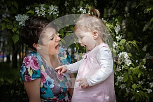 Mother and daughter have fun in the park and apple tree with white flowers