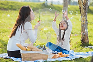 mother and daughter having fun blowing soap bubbles during a picnic