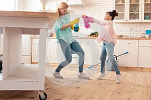 Mother and daughter having fun with cleaning spray in the kitchen