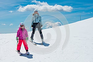 Mother and daughter having fun and learning skiing making first steps on a ski winter resort at mountain hill.