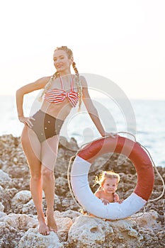 Mother daughter having fun resting on the rocky beach. Two blond lady wearing retro swimming suits enjoy summer day together