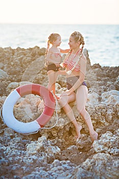 Mother daughter having fun resting on the rocky beach. Two blond lady wearing retro swimming suits enjoy summer day together