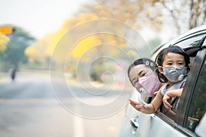 Mother and daughter having fun riding at the back of a car while wearing protective mask