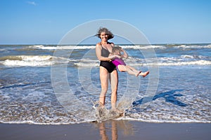 Mother and daughter having fun on sea beach on summer vacation. Family on sea rest. Happy people in swimwear on beach