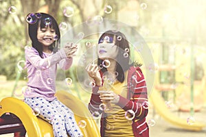 Mother and daughter having fun with soap bubbles at playground.