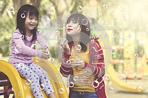 Mother and daughter having fun with soap bubbles at playground.