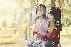 Mother and daughter having fun with soap bubbles at playground.