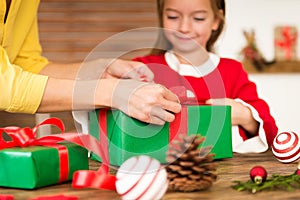 Mother and daughter having fun wrapping christmas gifts together in living room. Candid family christmas time lifestyle.