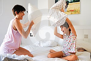 Mother and daughter having funny pillow fight on bed.