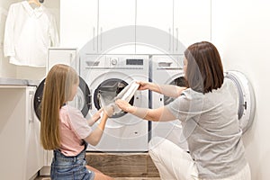 Mother and daughter helper in laundry room near washing machine and dryer pulling off clean clothes