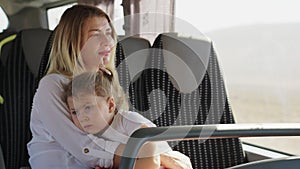 Mother and daughter in her arms are tired after a long journey in an empty bus