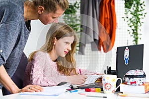 Mother and daughter during homeschooling. Young, blond girl in pink sweater is smiling and asking her mother to help her while