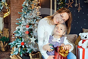 Mother and daughter hugging by the Christmas tree.