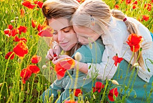 Mother and daughter hugging in a poppies meadow. Mom and child girl resting in the field with poppy flowers. Mother and
