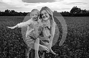 Mother and daughter hugging in a poppies meadow. Mom and child girl resting in the field with poppy flowers, piggyback