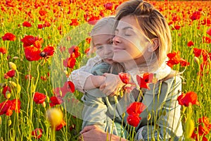 Mother and daughter hugging on spring blossom field. Mom with a child girl in a field of red poppies enjoys nature