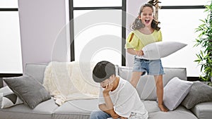 Mother and daughter jumping on sofa, disturbing home\'s relaxed atmosphere causes stressed mother to express comfort distress