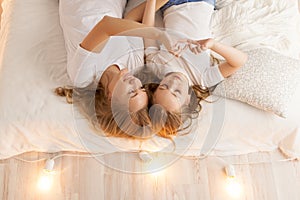 Mother and daughter lay on the bed and make heart by hands. View from above. Togetherness. Loft interior