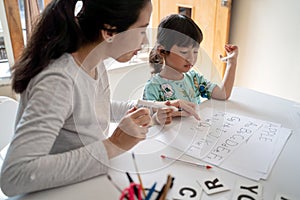 Mother and daughter learning to read and write letter at home