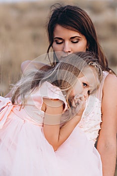 Mother and daughter look at the sea in pink dresses on the Sunset.