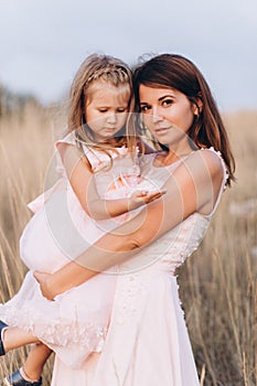 Mother and daughter look at the sea in pink dresses on the Sunset.