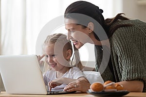 Mother daughter looking at laptop screen spend time in kitchen