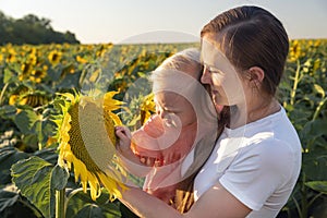 Mother and daughter are looking at a large sunflower flower on the field. Summer outside the city