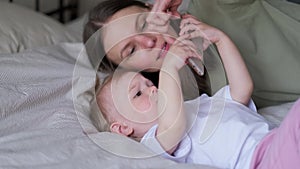Mother and daughter looking phone together on bed, Little baby girl and mommy playing at home