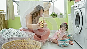 Mother & daughter love, smiling family doing laundry chores, talking together via smartphone video call in a cozy home laundry