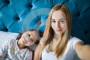 Mother and daughter lying on bed and taking self portrait with smartphone. Woman taking selfie on phone with a little girl in bedr