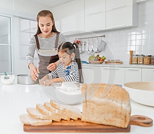 Mother and Daughter is making bakery in home kitchen counter together with bread on the foreground