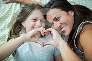 Mother and daughter making heart shape from hand while lying on bed