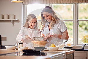 Mother And Daughter Making Pancakes In Kitchen At Home Together