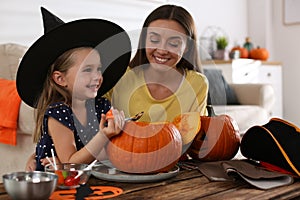 Mother and daughter making pumpkin jack o`lantern at table indoors. Halloween celebration photo