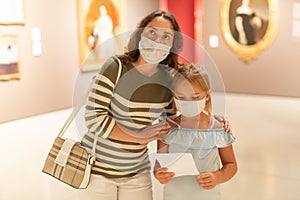 Mother and daughter in masks with guide enjoying expositions in museum