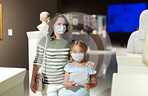 Mother and daughter in masks with guide enjoying expositions in museum
