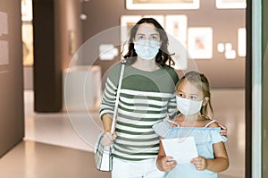 Mother and daughter in masks with guide enjoying expositions in museum