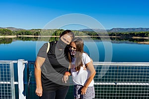 Mother and daughter with masks to protect themselves from the coronavirus posing in a lake with the forest reflected in the water