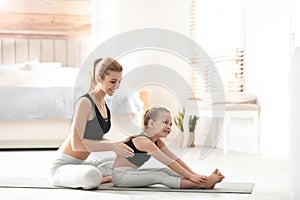 Mother and daughter in matching sportswear doing yoga near bed at home